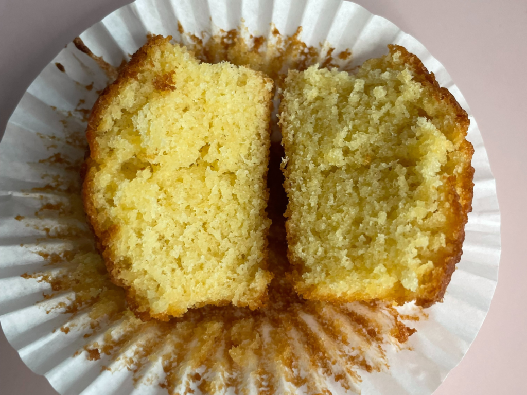 A vanilla cupcake cut in half an open on a white cupcake case on top of a pink plate. To show that the cake is cooked.